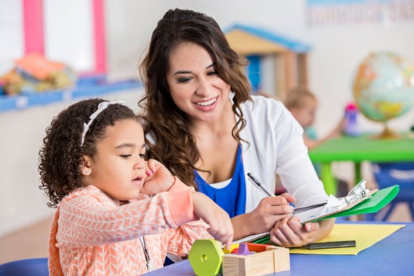 Teacher assessing young girl as she completes a puzzle.