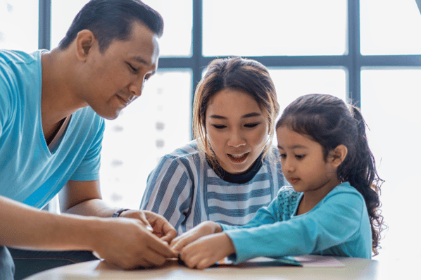 Mom and dad help their young daughter with an art project in the classroom.