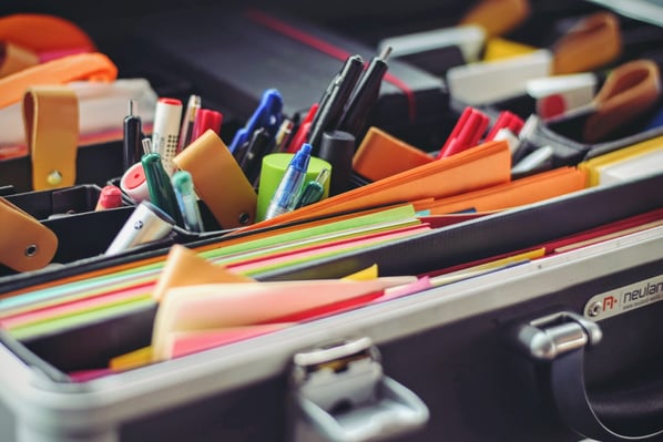 A file folder with multiple papers, pens, and other office supplies.