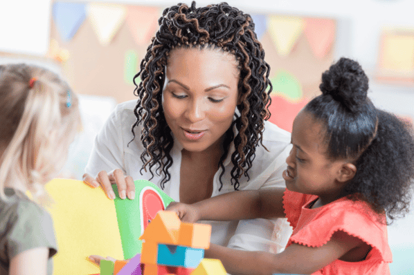 Preschool teacher plays blocks with student in classroom