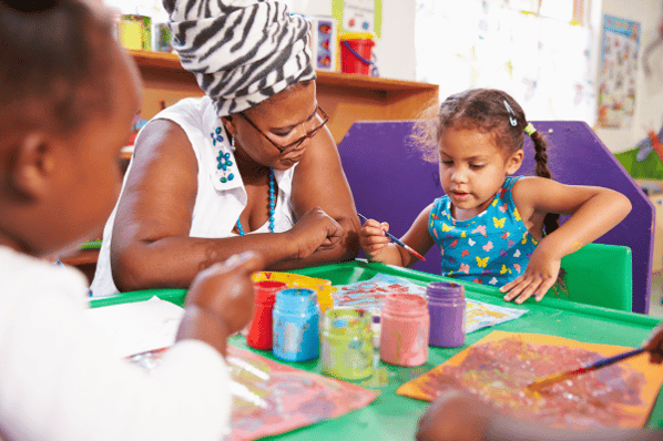 Teacher painting with child in preschool.