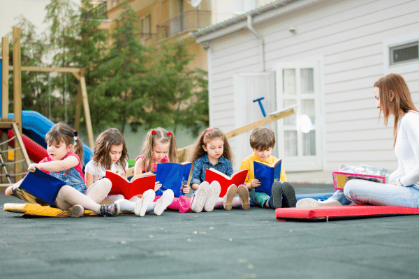 Teacher and preschool children sitting outside on the playground each reading a picture book