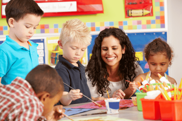 Preschool children painting at a table with their teacher