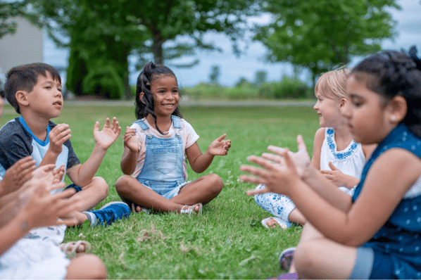 Preschool circle sitting in a circle outside, clapping their hands.