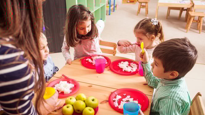 Children are having snacks at a table in a daycare center.