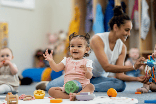 Toddlers sitting on floor at daycare with teacher.