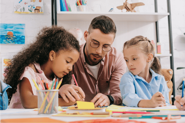 Male teacher helping two young girls with an art project