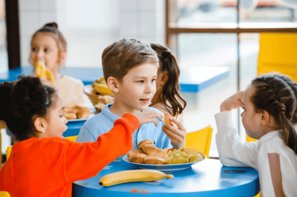 Three children sitting at a table eating healthy snacks together.