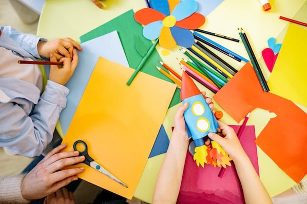 Children sitting at a yellow table doing project-based learning using arts and crafts such as colored pencils and paper.