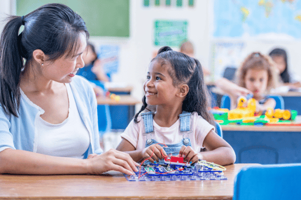 happy teacher and student sitting at a desk, looking at each other and smiling