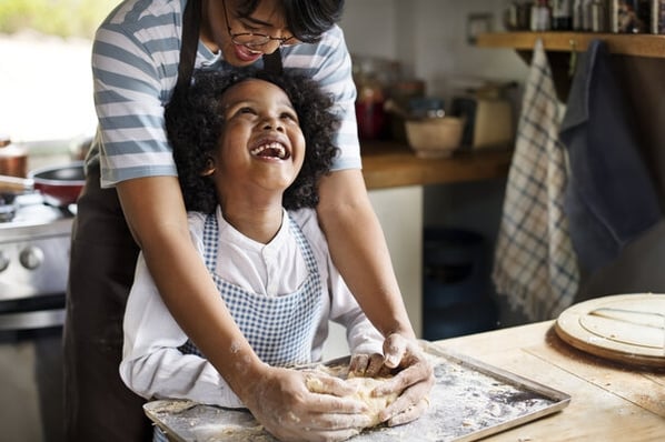 Young child with parent in the kitchen kneading dough on a baking sheet.