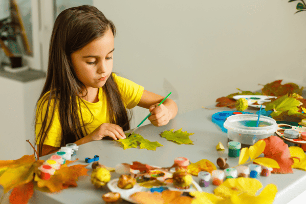 Little girl painting on yellow leaves for an art project.