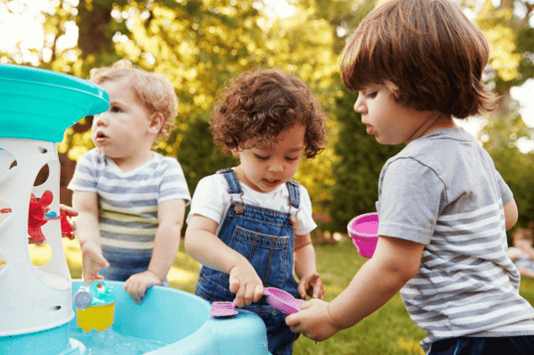 Preschool children playing with water table outside.