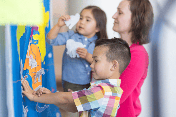 Two children and woman kneeling in front of a poster of the earth and sticking animal pictures on it.