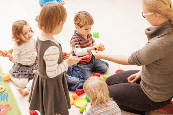 Teacher sitting with group of preschool children playing with plastic toy fruit.