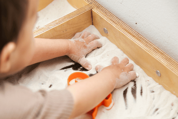 Closeup of toddler playing in kinetic sand sensory bin.