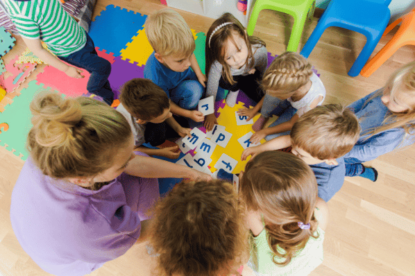 Teacher with children at daycare doing a letter recognition activity with flashcards.