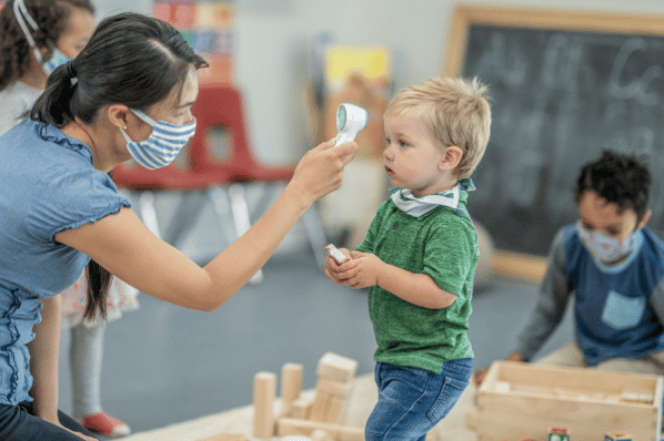 Teacher checks a child's forehead temperature at daycare.