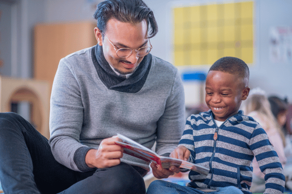 Male teacher reading a picture book to young child.